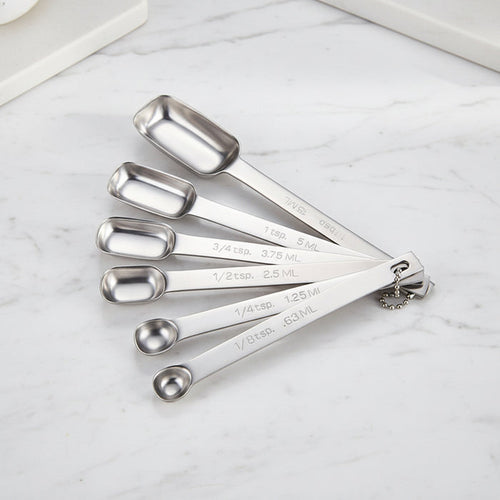 Six-piece stainless steel measuring spoon set arranged on a white marble surface