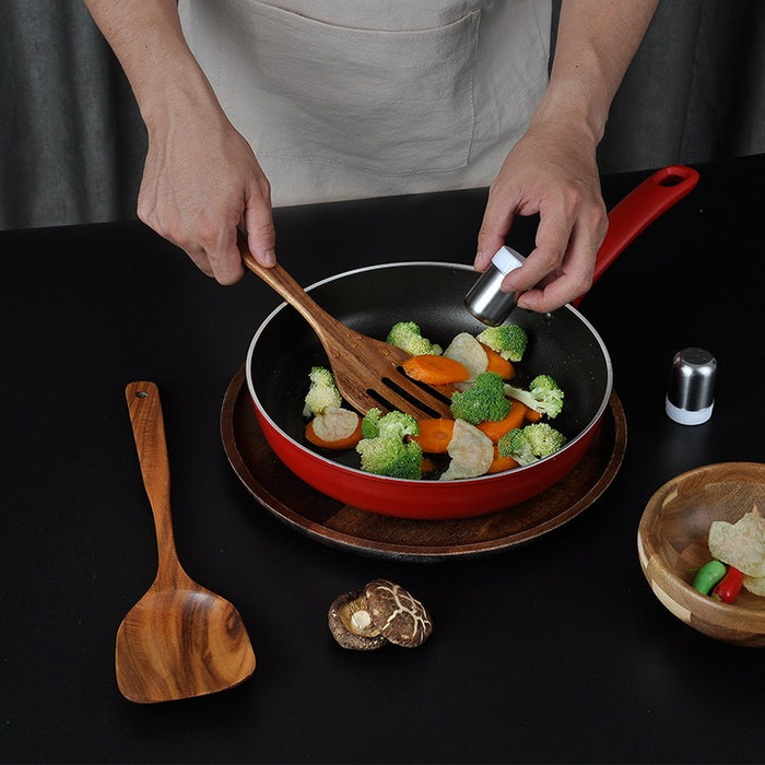 Wooden slotted spatula being used to cook vegetables in a frying pan