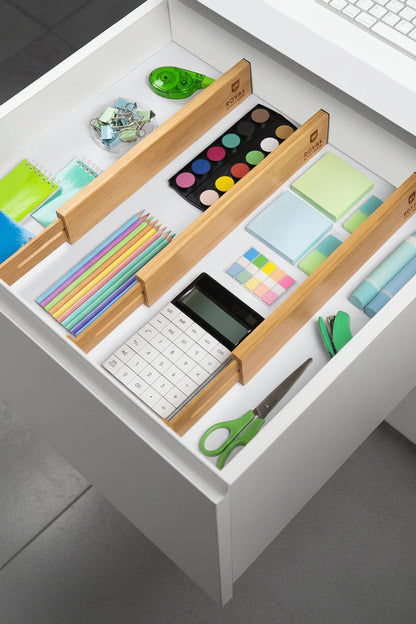 Adjustable bamboo drawer dividers organizing office supplies inside a white desk drawer