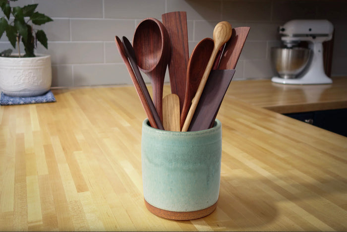 Set of wooden spoons in a green ceramic holder on a kitchen counter.