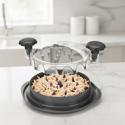 Black manual chicken shredder with handles and clear lid filled with shredded chicken