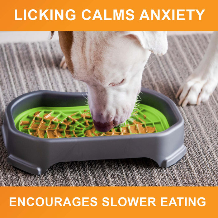 Dog licking peanut butter from the purple Neat-Lik Mat Slow Feed Licking Mat with text that reads "Encourages slow eating and reduces anxiety."