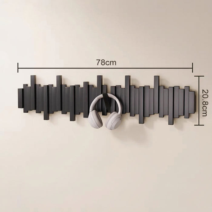 Black wooden wall mounted coat rack with hooks holding white headphones in an entryway