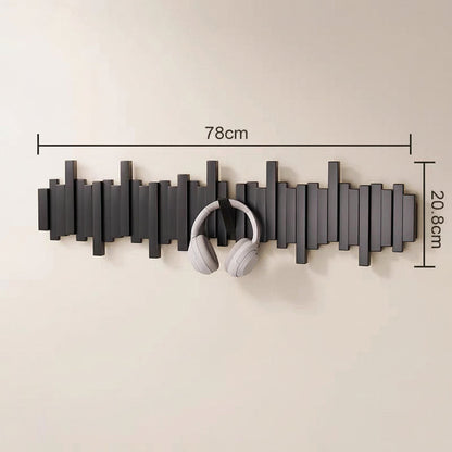 Black wooden wall mounted coat rack with hooks holding white headphones in an entryway