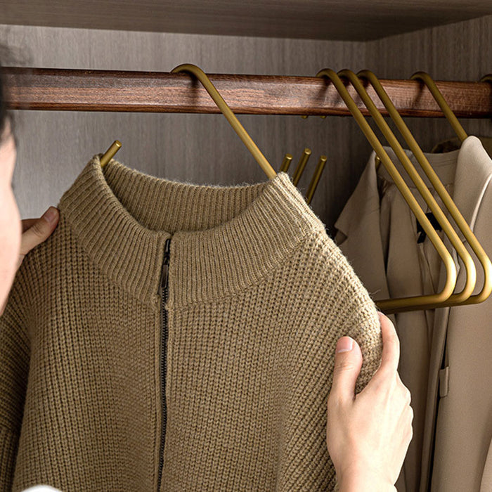 Person removing a sweater from an open-ended gold pants hanger in a closet
