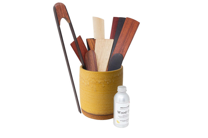 Set of wooden utensils in a yellow holder with a bottle of wood oil on a white background